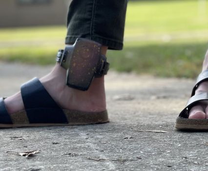 A close up of an ankle monitor on a person wearing sandals