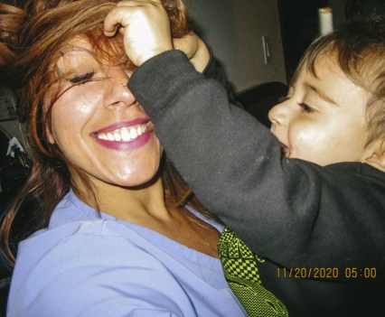 A woman smiling and holding a young child who is playing with the woman's hair
