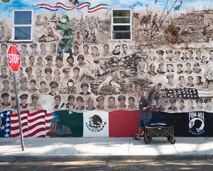 A mural on the side of a building with vintage photos of soldier's faces and large Mexican and US flags