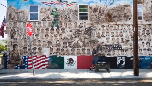 A mural on the side of a building with vintage photos of soldier's faces and large Mexican and US flags