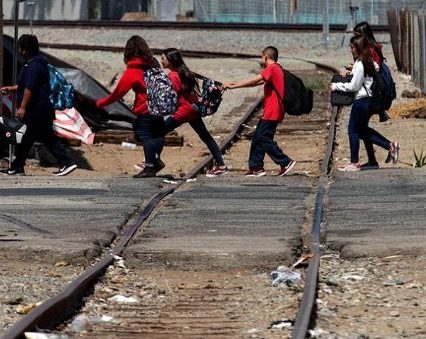 A group of children in red and black uniforms crossing train tracks on the way to school