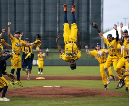 A baseball team in all yellow uniforms cheer on a teammate doing a flip