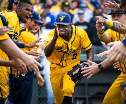 A baseball player in all yellow runs towards the camera, team members on both sides
