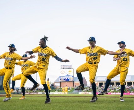 A small group of baseball players in all yellow are on the baseball field performing a dance