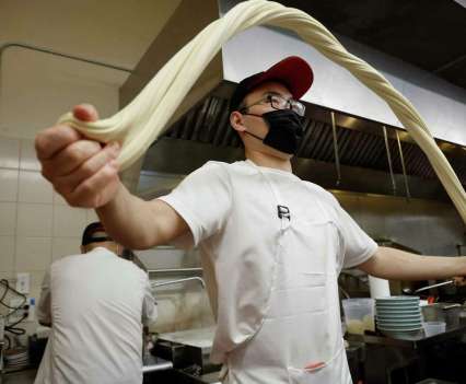 A chef in a mask stretching dough