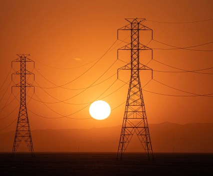 The sun sets behind a row of electric towers in Fresno County