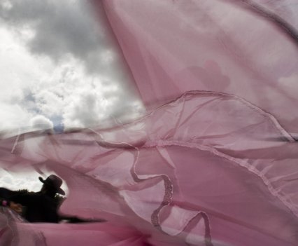 Dancers surrounded by floating pink material against a cloudy sky