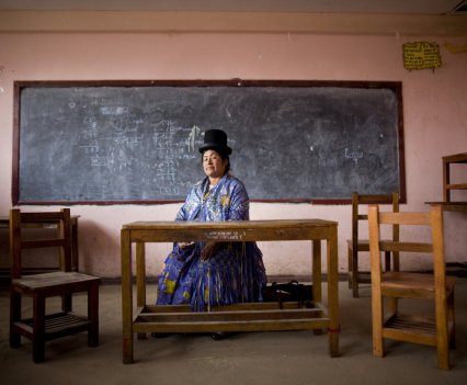 Woman sitting at a desk in a classroom in front of a chalkboard