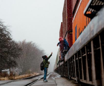 One child helps another cross over a parked freight train blocking their route to school.