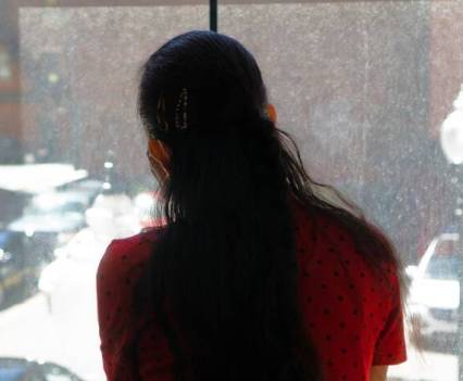 A woman with long, dark hair is looking out a window