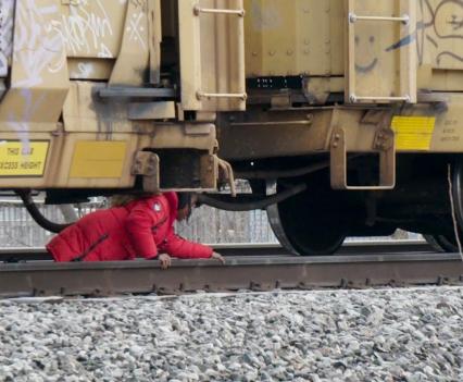 A child in a red coat crawls under a parked train