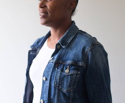 A woman in a jean jacket stands against a white background