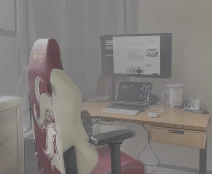 A computer on a desk with an office chair in front sit in a smoky room