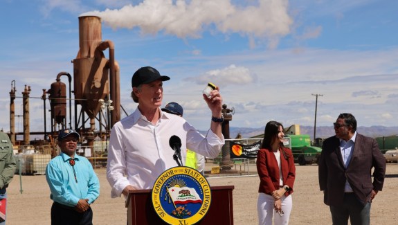 Photo of a politician speaking from behind a podium on the site of an industrial plant