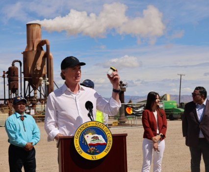 Photo of a politician speaking from behind a podium on the site of an industrial plant