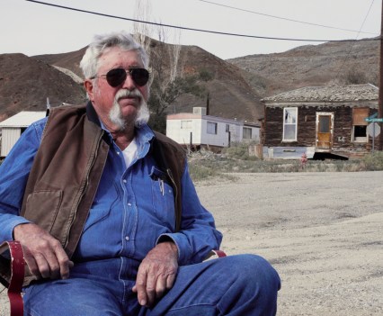 Photo of a man with sunglasses and a beard sitting outside in a dry, desert environment