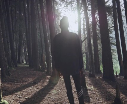 Photo of a female figure in the woods with light shining through the trees