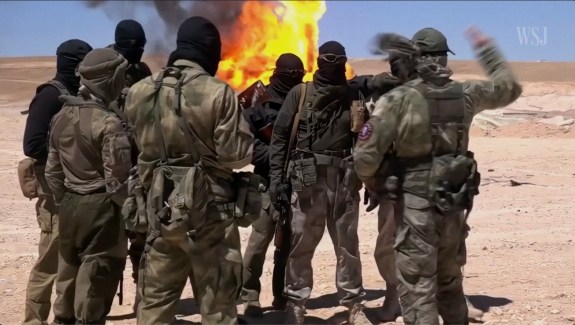 Photo of a group of military men with black masks on in front of a fire