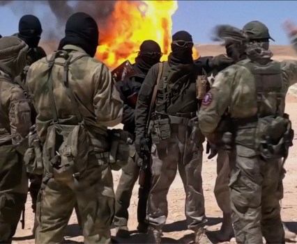 Photo of a group of military men with black masks on in front of a fire