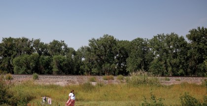 Photo of a women in a white shirt and pink skirt walking away from a cross in the middle of a field