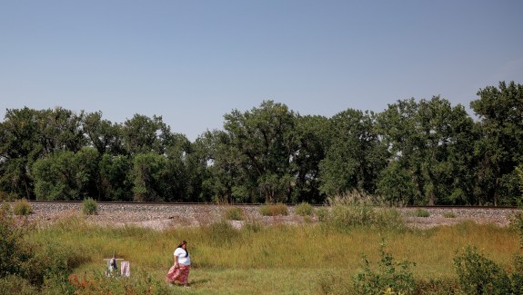 Photo of a women in a white shirt and pink skirt walking away from a cross in the middle of a field