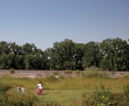 Photo of a women in a white shirt and pink skirt walking away from a cross in the middle of a field