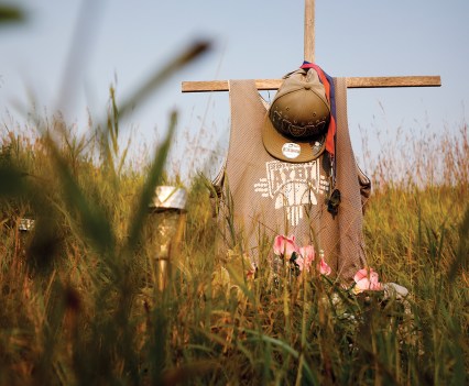 Photo of a cross in a field with a hat and shirt laid across the cross