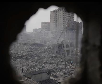 Black and white photo inside of a the hole in a wall showing a destroyed cityscape on the other side