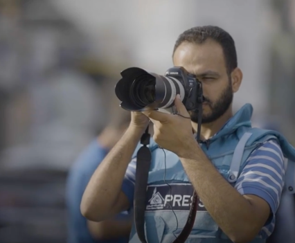 Photo of an Arab man holding a video camera up to his eyes