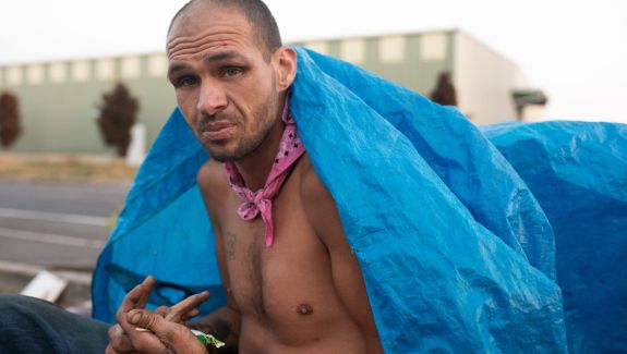 Photo of a man without a shirt on covering his back with a blue tarp