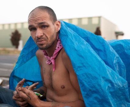 Photo of a man without a shirt on covering his back with a blue tarp