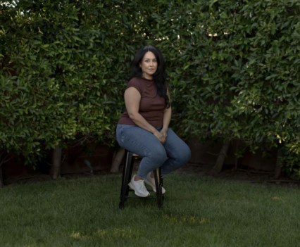 Woman in brown shirt and blue pants seated in green outdoor space