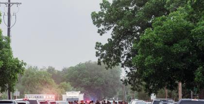 Street lined with cars with group of people including police officers in the middle of the street