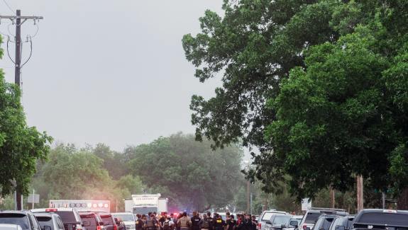 Street lined with cars with group of people including police officers in the middle of the street