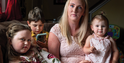 A blond woman holds a toddler on her lap. She is sitting next to two other children