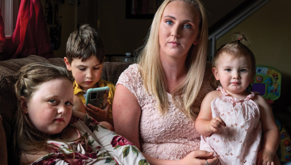 A blond woman holds a toddler on her lap. She is sitting next to two other children