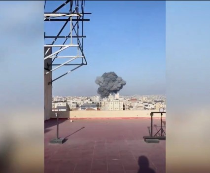 Photo of a large cloud of smoke rising from buildings in a distant city