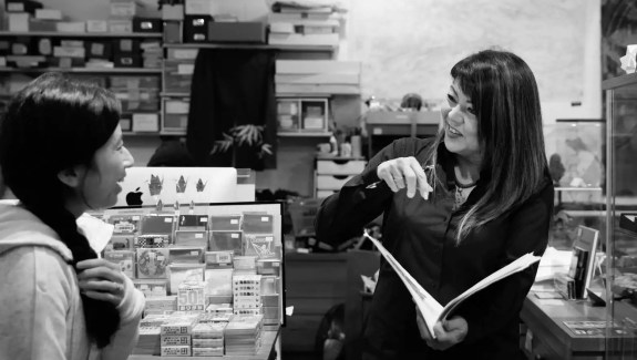 Black and white image of a woman holding an open book in a store