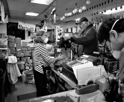 A woman in a mask rings up a purchase for a man on the other side of a counter in a store