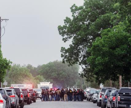 Cars line both sides of the street and a crowd of people are gathered at the far end of the street