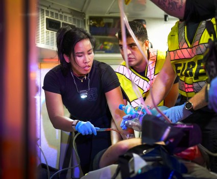 Three emergency responders work to administer blood to a patient