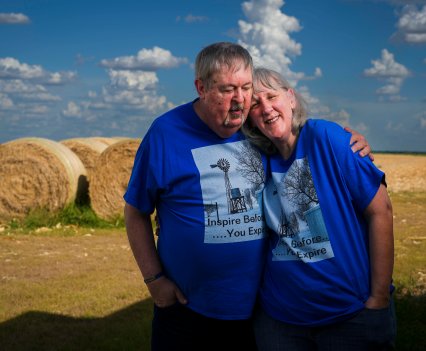 A man has his arm around a woman in a field. They are wearing matching blue shirts