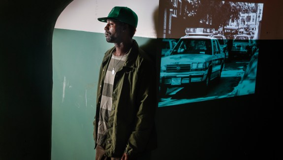 DonJuan Moses, next to a projection of police cars in Mission Hill after the Stuart shooting. DonJuan was 11 years old when police burst into his Mission Hill home and arrested his cousin.