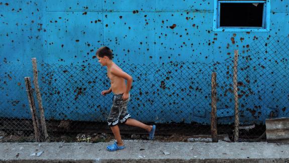 Cousin Oleksandr running in front of the Kolotylos’ shed that is full of damage from the war.