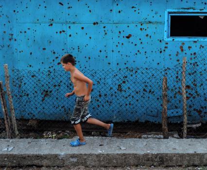 Cousin Oleksandr running in front of the Kolotylos’ shed that is full of damage from the war.