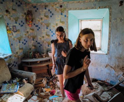 Two young teen girls walk carefully through the debris in their home after it is destroyed by occupying forces