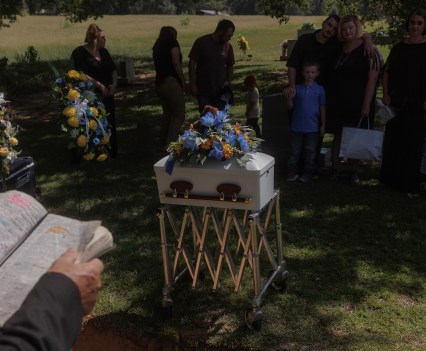 A pastor reads from the bible as family and loved ones gather and embrace each other around the casket carrying Perseus and Helios Langley at a burial in Broken Bow, Oklahoma on August 18, 2023.