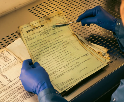 Gloved hands hold a fire damaged document