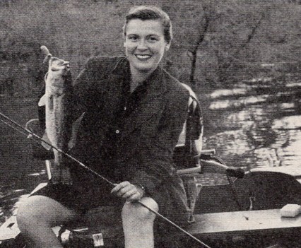 Virginia Kraft holds up a bass, smiling, in a small fishing boat.