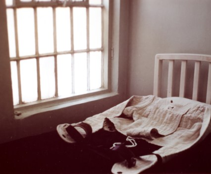 A photo of what appears to be a straitjacket lying on a bed by a window.